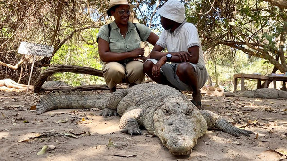 The writer gets extremely close to one of the crocodiles at Kachikally Crocodile Pool and Museum alongside Moses Bajo, a park spokesperson and croc caretaker.